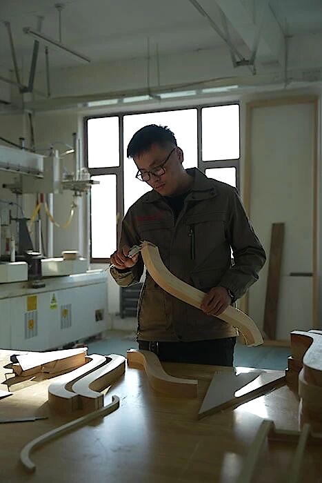 Worker inspecting a curved wooden component above a bench of similar pieces