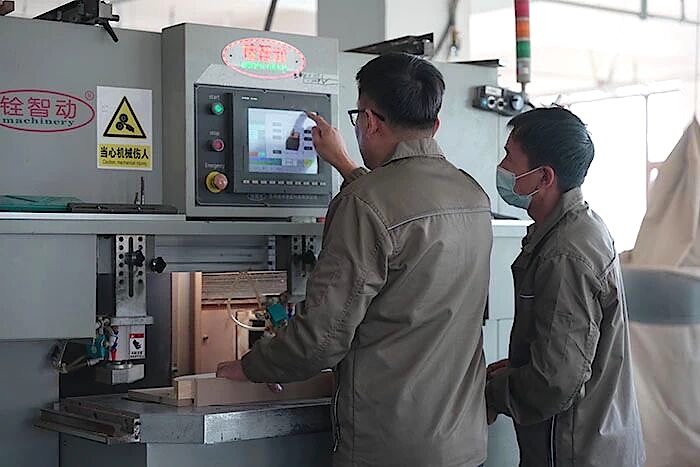 Two workers operating a woodworking machine with a wooden component beneath its controls