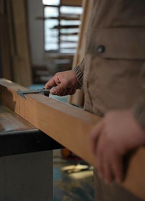 Hands using calipers to measure the edge of a wooden component