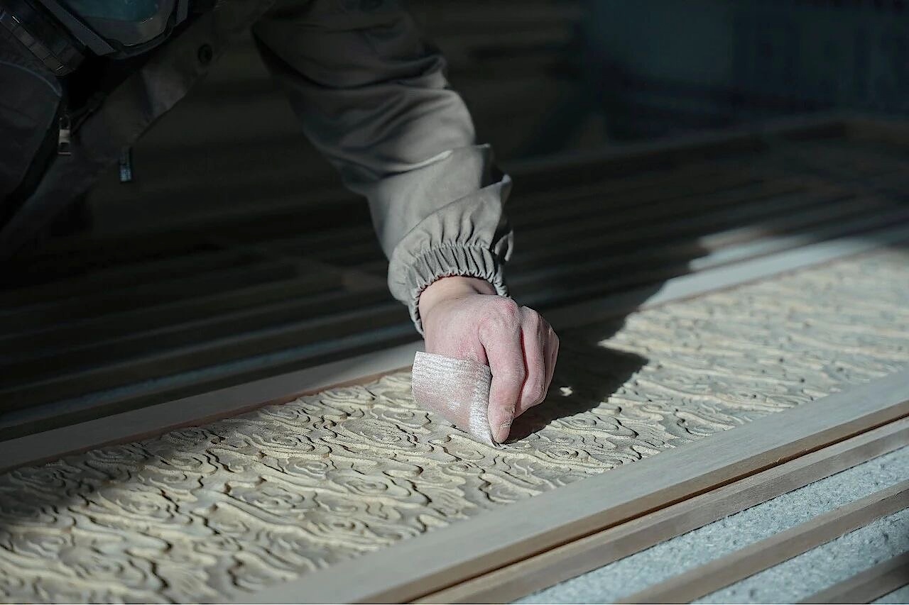 Hand sanding the raised decorative pattern of a carved wooden panel