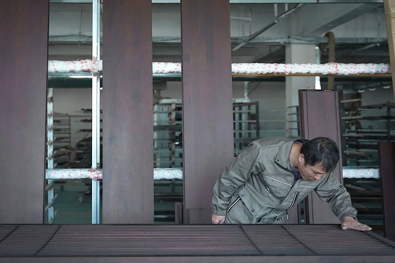 Worker leaning over a dark wooden slatted panel while touching its surface