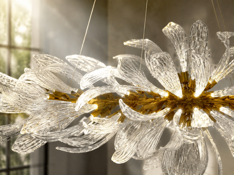 Close-up of textured glass leaves branching from a golden-toned chandelier frame in sunlight