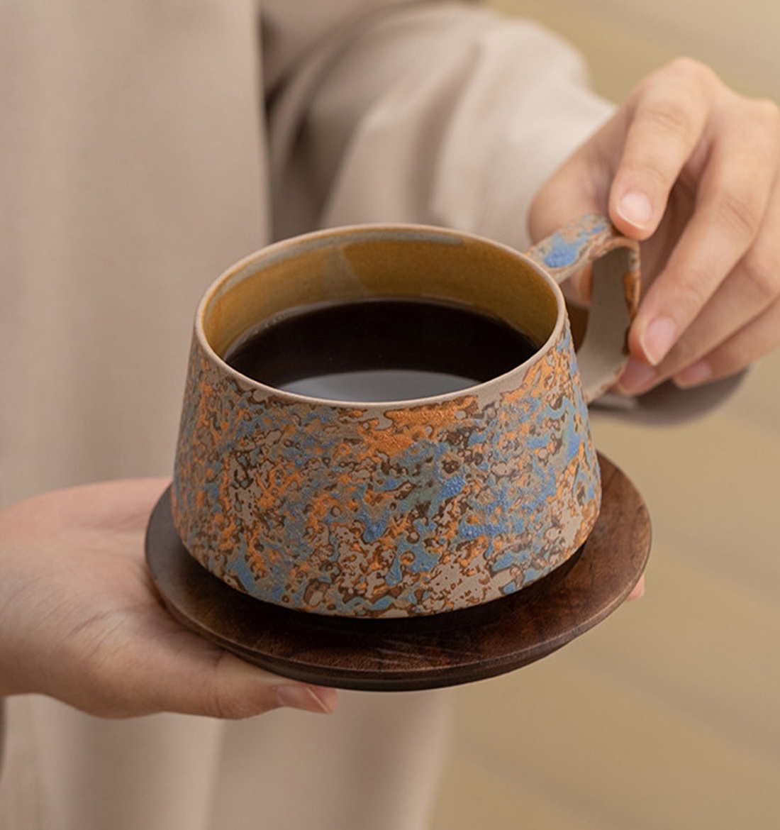 Mix Blue mottled cup filled with coffee, held by its angular handle above a dark wooden saucer