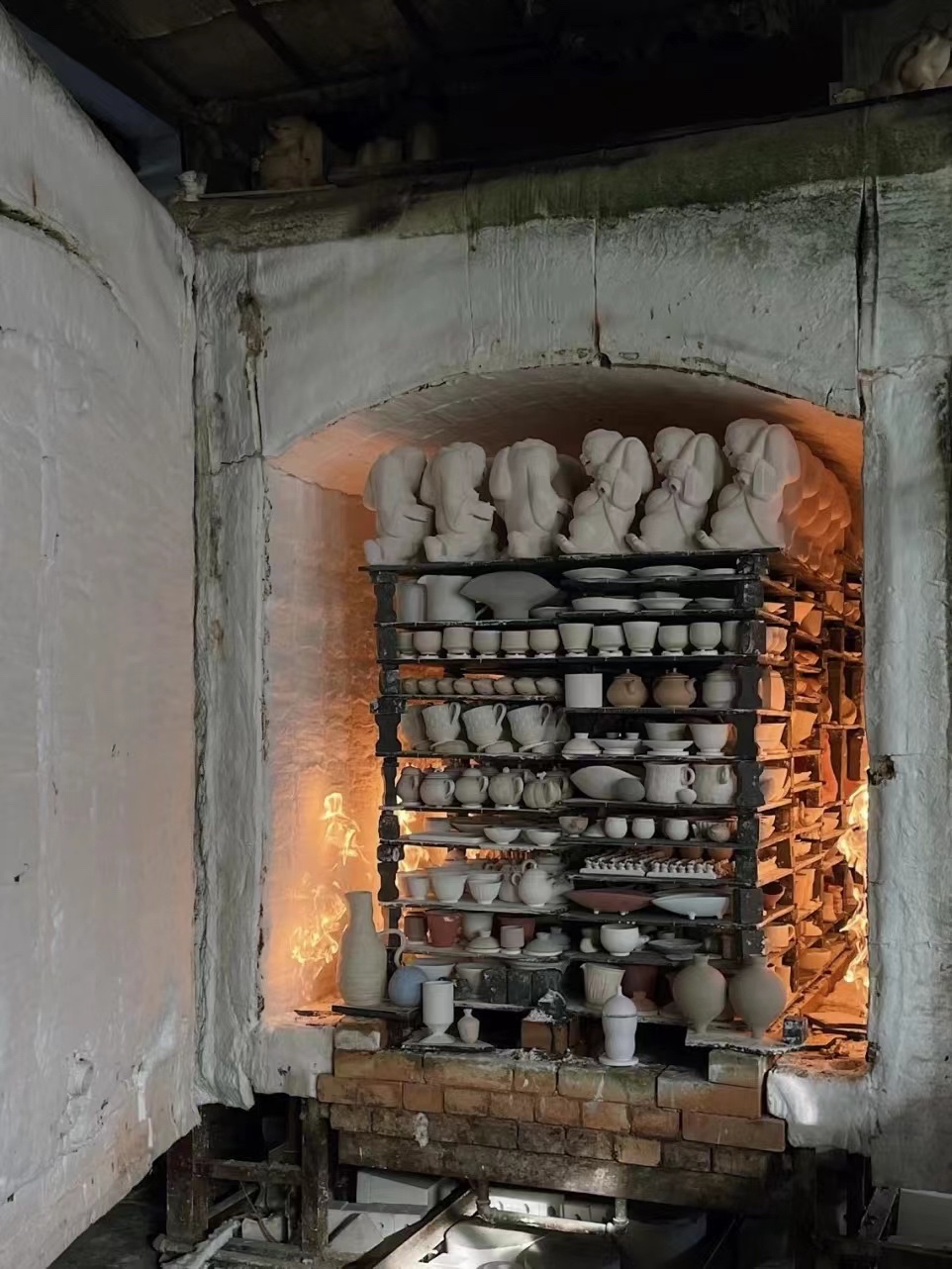 Open kiln filled with shelves of cups, bowls, and ceramic figures