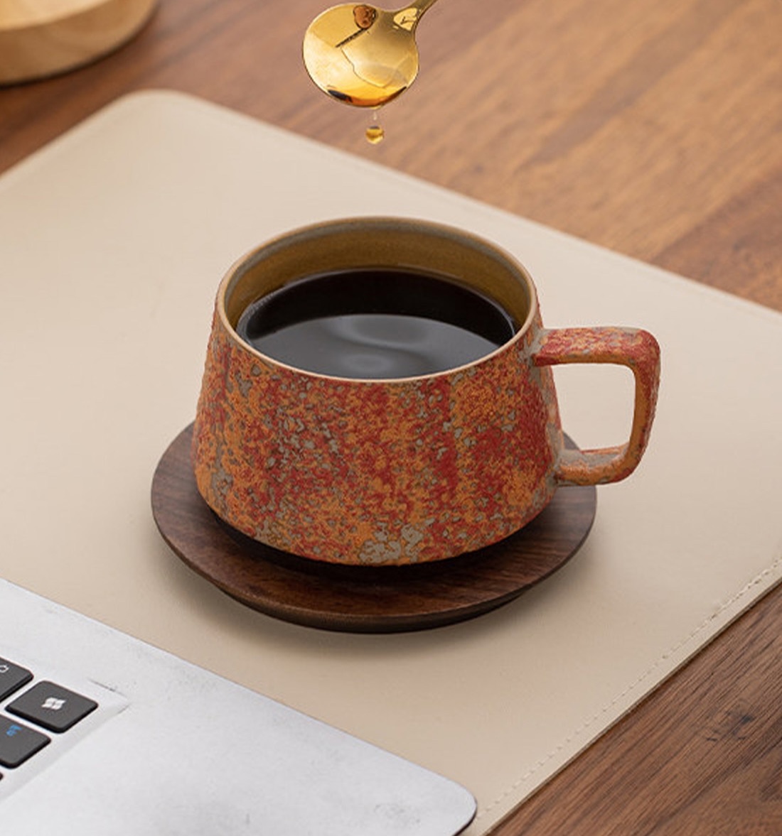 Dawn Red cup of coffee on a wooden saucer beside a laptop and beneath a gold spoon
