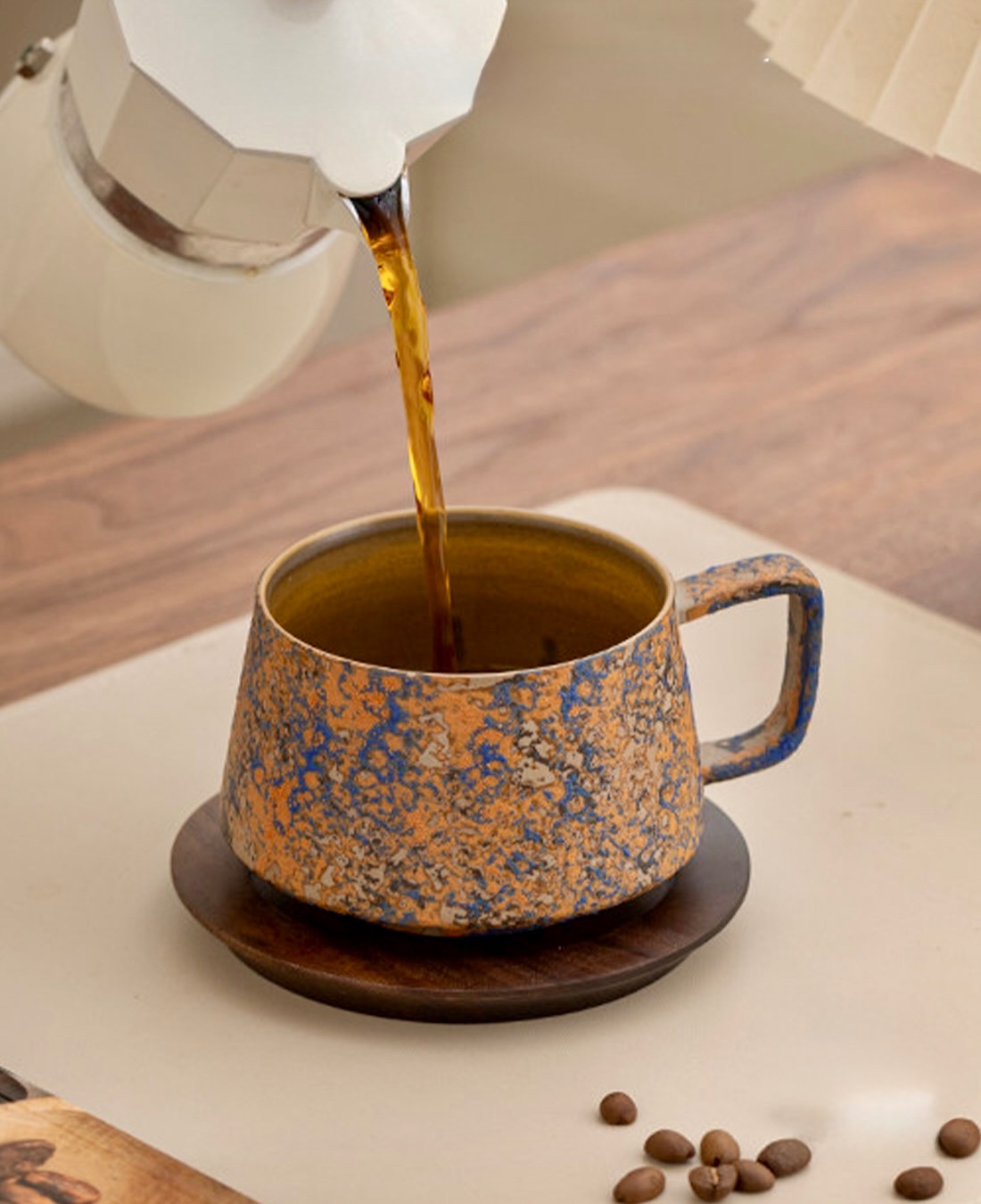 Coffee poured from a white moka pot into an ochre and blue mottled cup