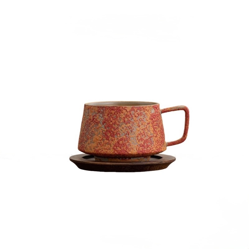 Dawn Red cup with red and ochre speckles and an angular handle on a wooden saucer