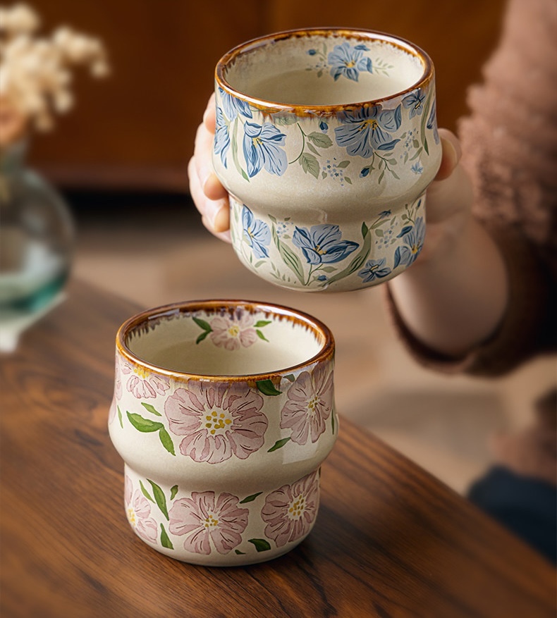 Blue floral cup held above a pink floral cup on a wooden table