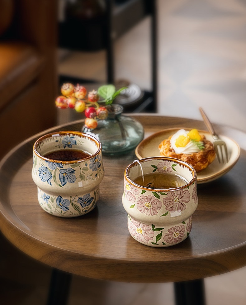 Blue cup of coffee and pink cup of tea beside a pastry on a round wooden table