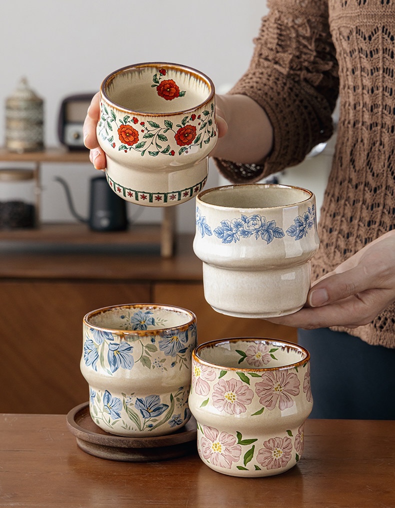 A person holding red and blue floral cups above blue and pink cups on a table