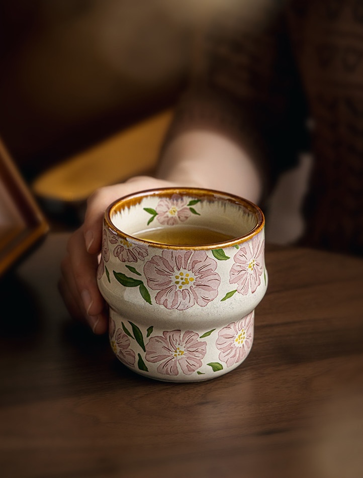 Blush Petal cup of tea held on a wooden table, showing pink flowers and its stepped shape