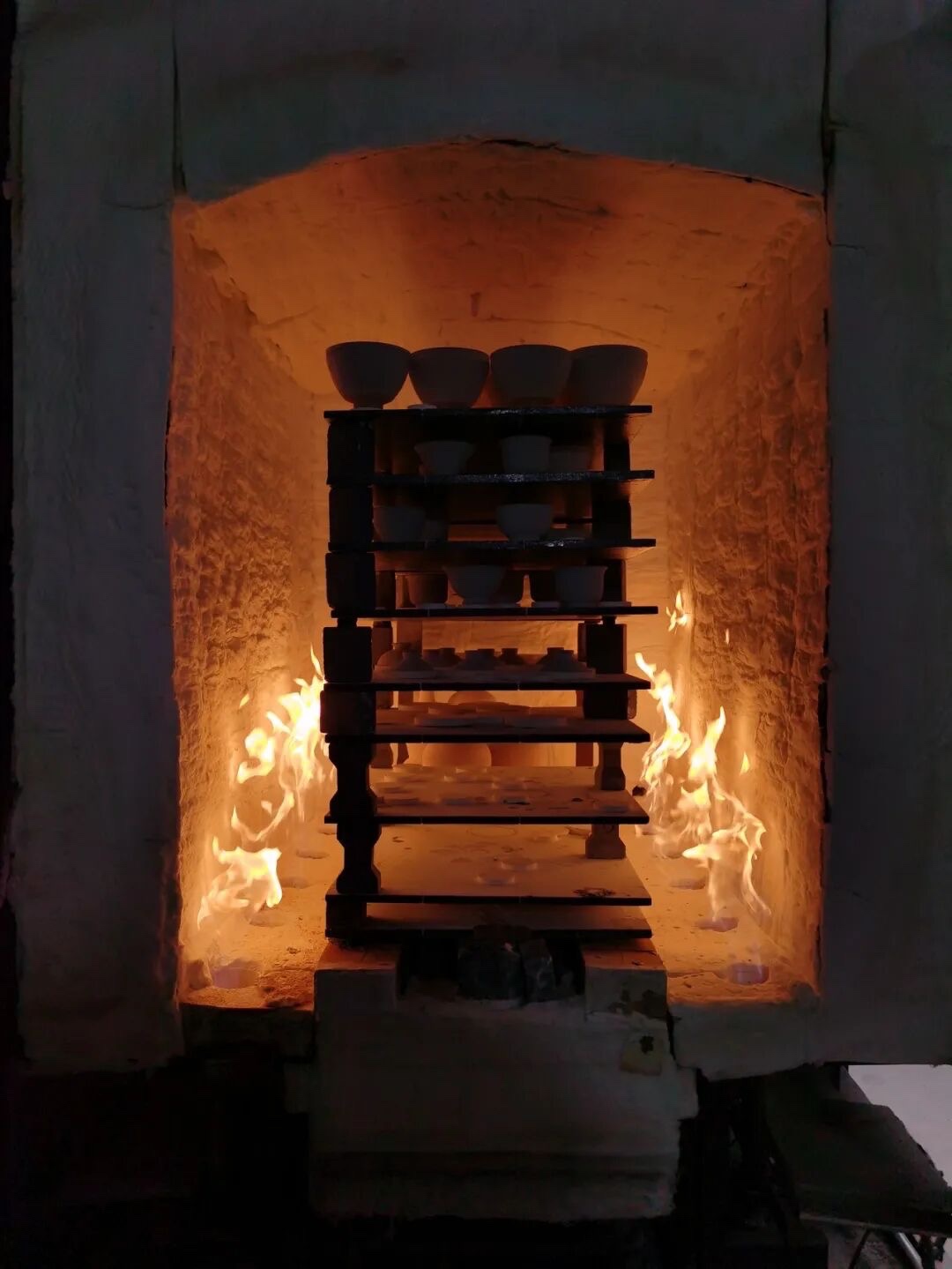 Ceramic vessels arranged on shelves inside a glowing kiln