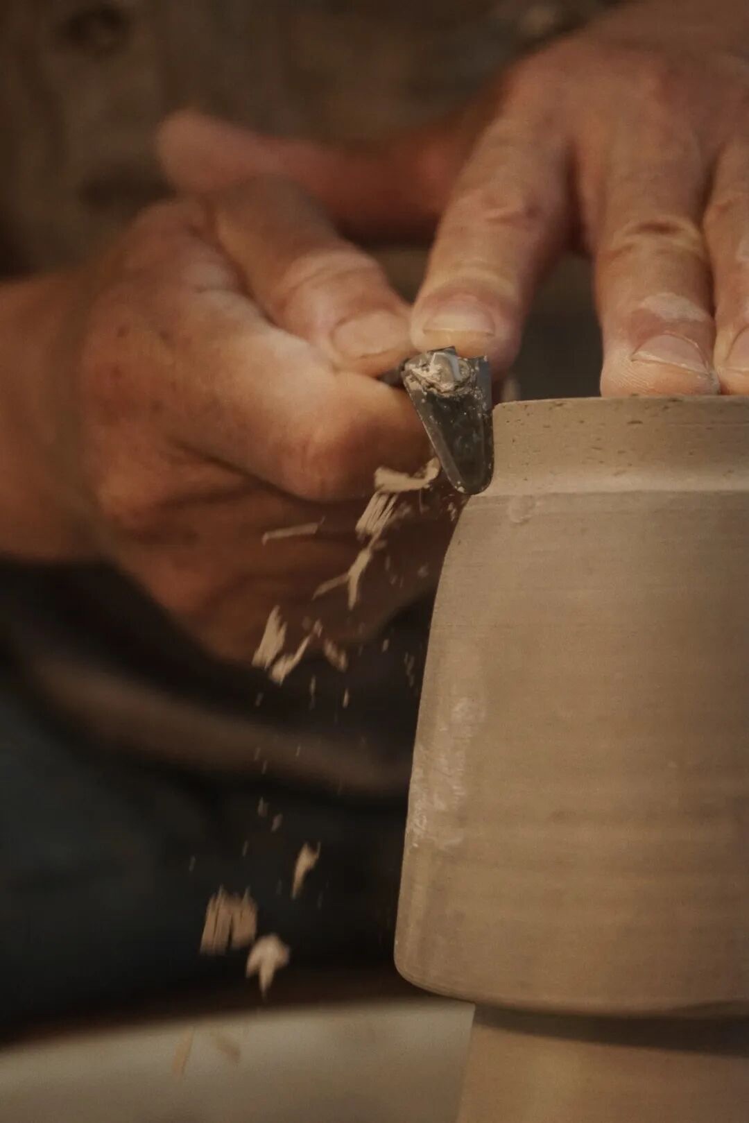 Hands trimming the base of a clay vessel with a pottery tool