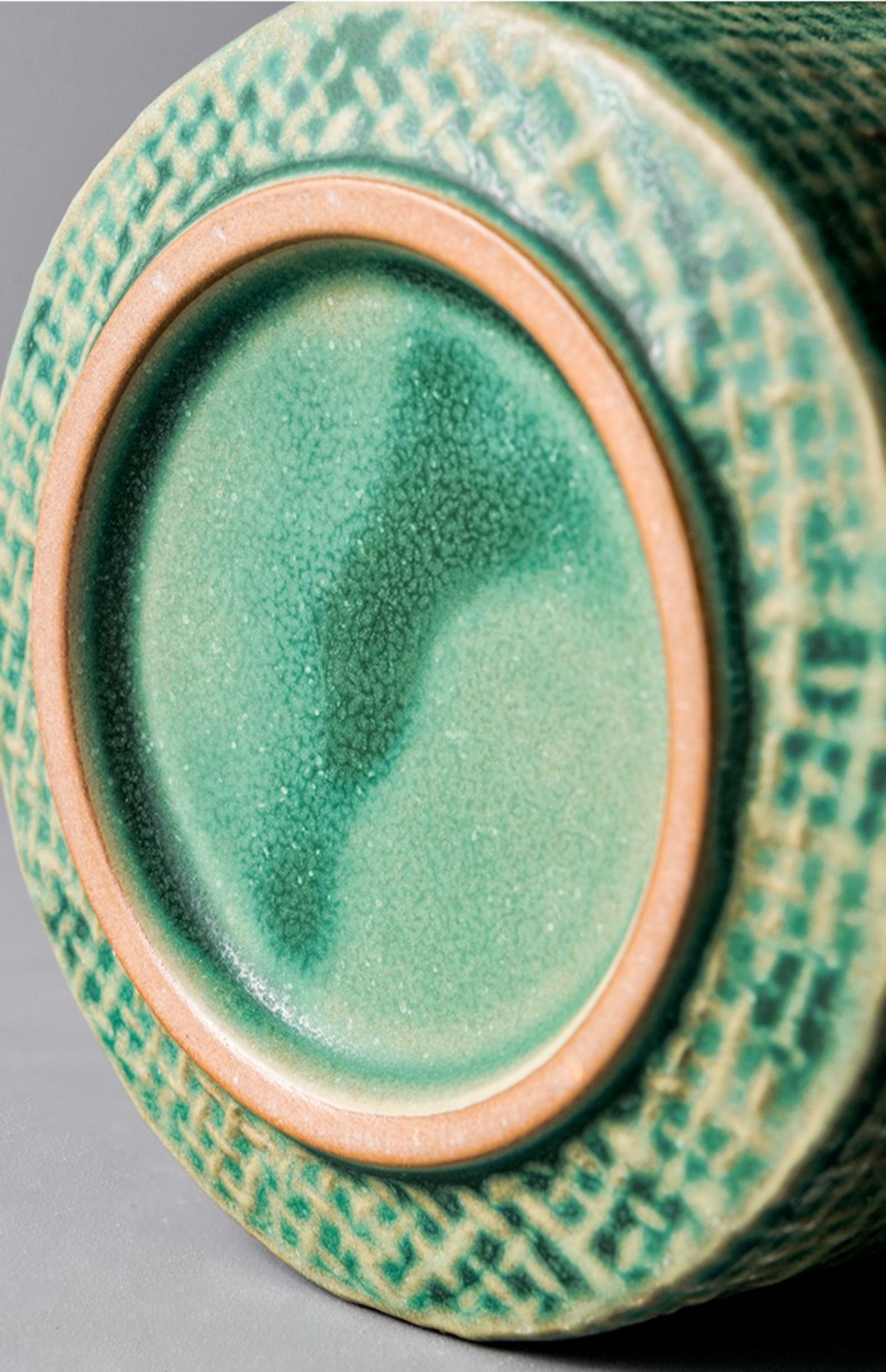 Close-up of the green glazed cup base, exposed clay foot ring, and crosshatched exterior