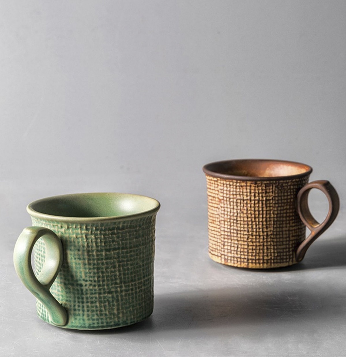 Moss Green and Toasted Amber cups showing their loop handles and linen-like surface texture