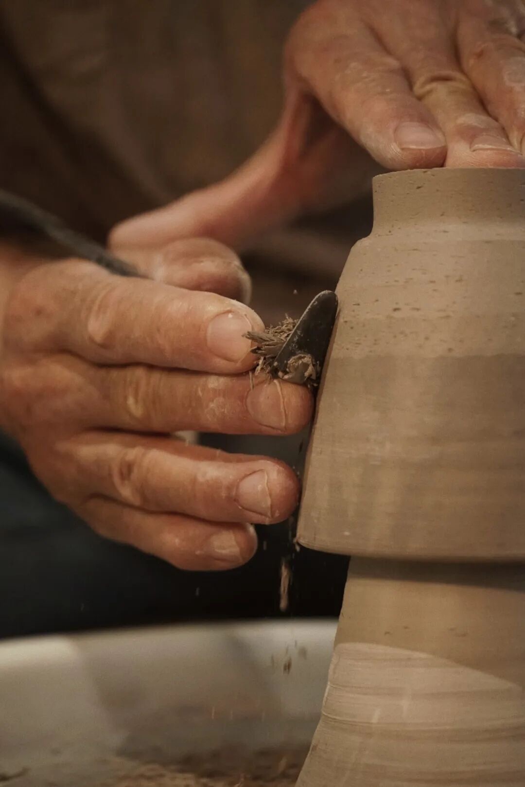 Hands trimming the outside of an inverted clay vessel on a pottery wheel