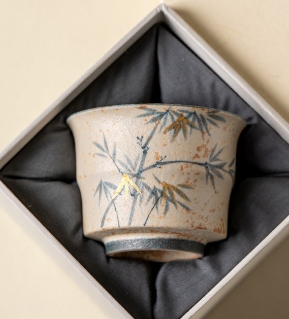 Bamboo-decorated tea cup displayed in an open box with dark fabric lining